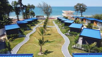 A resort with multiple blue-roofed buildings arranged in a curved layout, a central pathway, and a view of the sea.