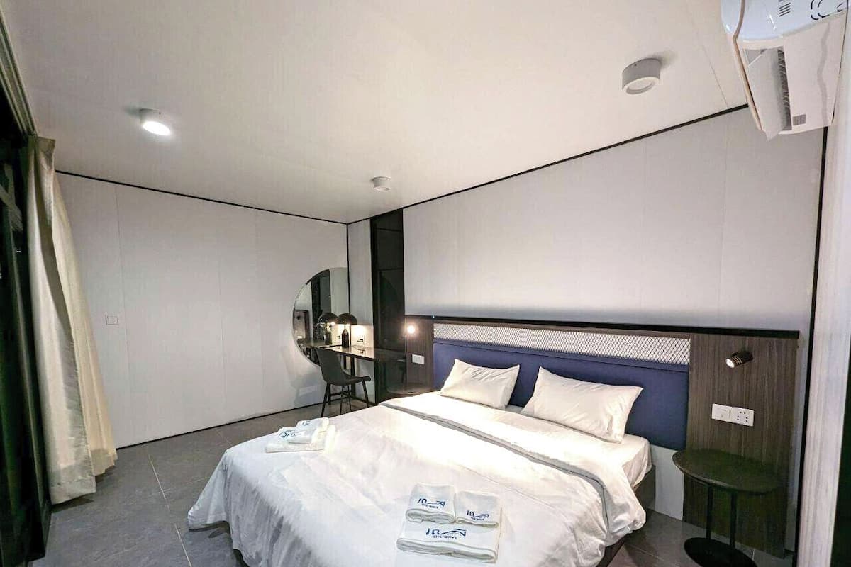 A modern hotel room with a neatly made bed, a desk with a chair, and a small table.