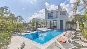Ein moderner Poolbereich mit rechteckigem Pool, Liegestühlen und einem zweistöckigen Gebäude mit großen Fenstern.