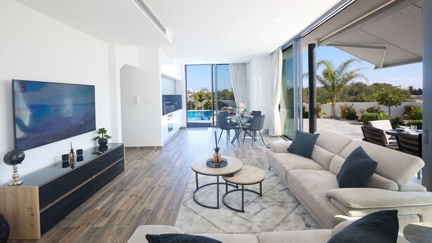 Ein modernes Wohnzimmer mit einem großen Flachbildfernseher, einer Couch, einem Couchtisch und einem Essbereich mit einer Glastür zum Balkon.