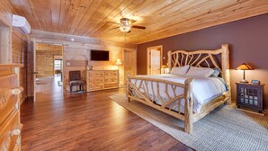 Quarto de cabana de madeira com cama, ventilador de teto, televisão e mesa de cabeceira.
