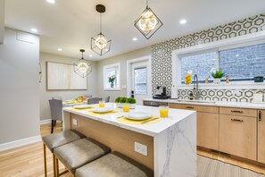Et moderne køkken med en central ø, hængende lamper og et mønstret backsplash.