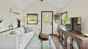 A living room with a white sofa, a coffee table with a basket, a TV on a wooden cabinet, and a door with windows. - New Tiny Home W/Mountain Views (Weaverville)
