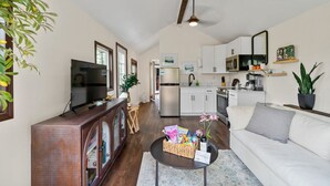 A living room with a sofa, coffee table, and TV. There is a kitchen area with cabinets and appliances. - New Tiny Home W/Mountain Views (Weaverville)