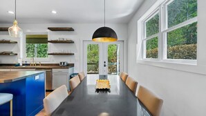 Een moderne keuken met een centraal eiland, een eethoek met een lange tafel en grote ramen met uitzicht op de omgeving.