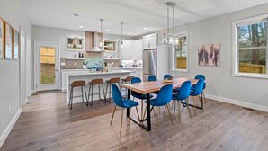 Une cuisine moderne avec des meubles blancs, un îlot central et des chaises bleues disposées autour d’une table en bois.