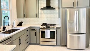 A modern kitchen with a stainless steel stove, oven, and refrigerator, light grey cabinets, and a black range hood. - 3 bedroom East Hill home 1 block from Bayview Park (Pensacola)