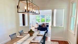 A dining room with a long wooden table, chairs, and a chandelier. There is a window with a view of greenery outside. - 3 bedroom East Hill home 1 block from Bayview Park (Pensacola)