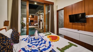 A hotel room with a bed, a television, and a view of a pool area. - Villa Casa Natura 15 (Ubud)
