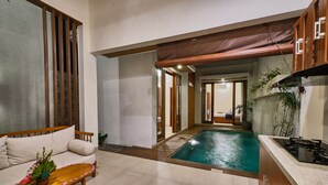 A modern kitchen with a built-in stove, a dining area with a wooden table and chairs, and a small pool area. - Villa Casa Natura 15 (Ubud)
