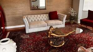 A living room with a tufted sofa, a glass coffee table with a golden statue, and a red armchair. - Isoyi on the Mill (Durban North)