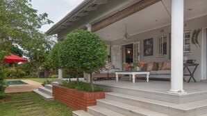 A covered porch with a seating area, steps leading to the entrance, and a small garden with a tree and a red umbrella. - Isoyi on the Mill (Durban North)