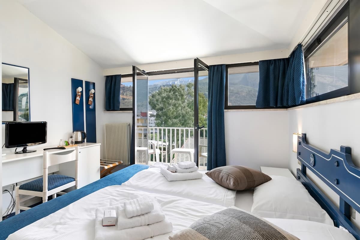 A hotel room with a bed, a desk, a TV, and a balcony with a view.
