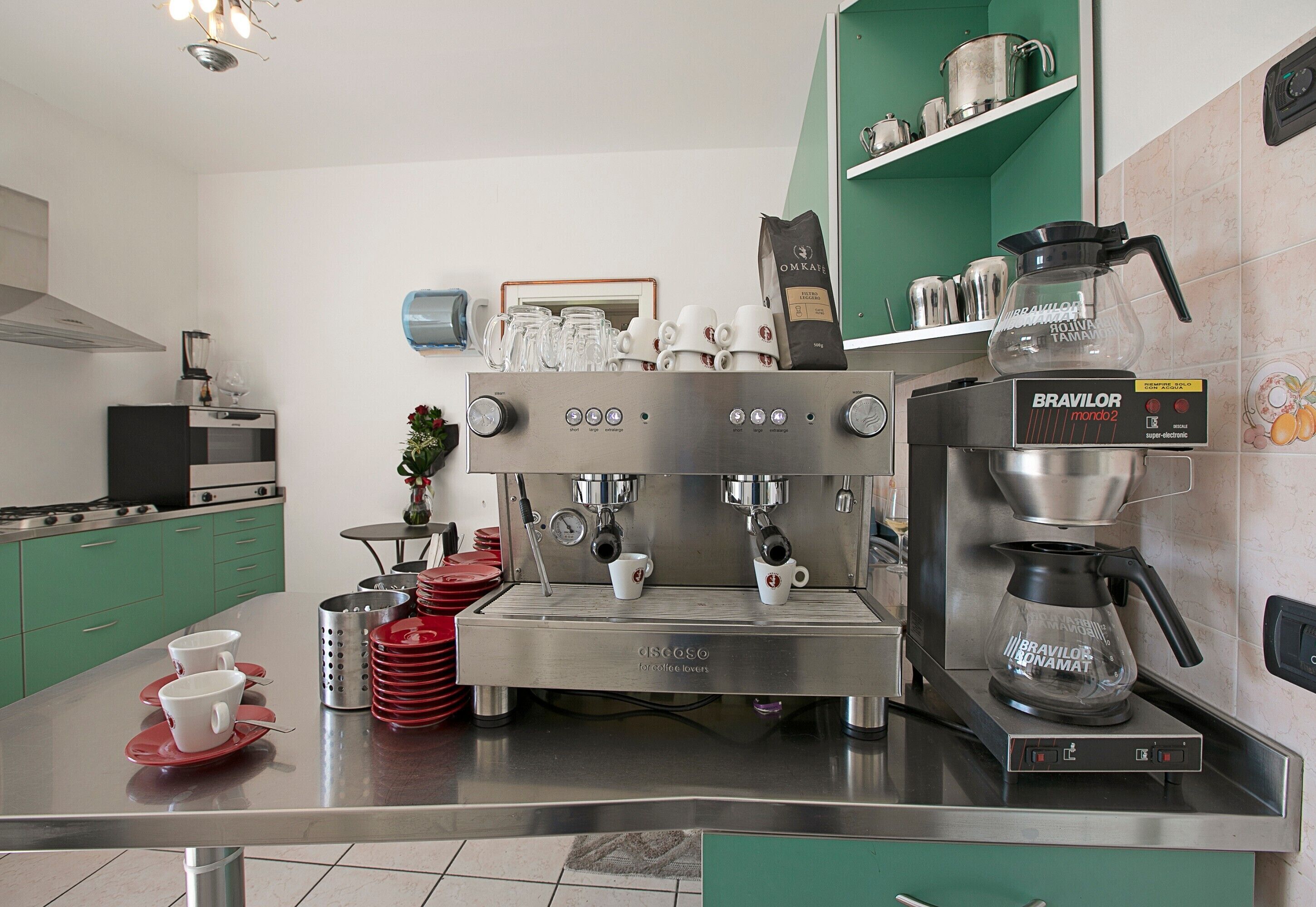 A modern kitchen with a coffee machine, green cabinets, and a coffee pot.
