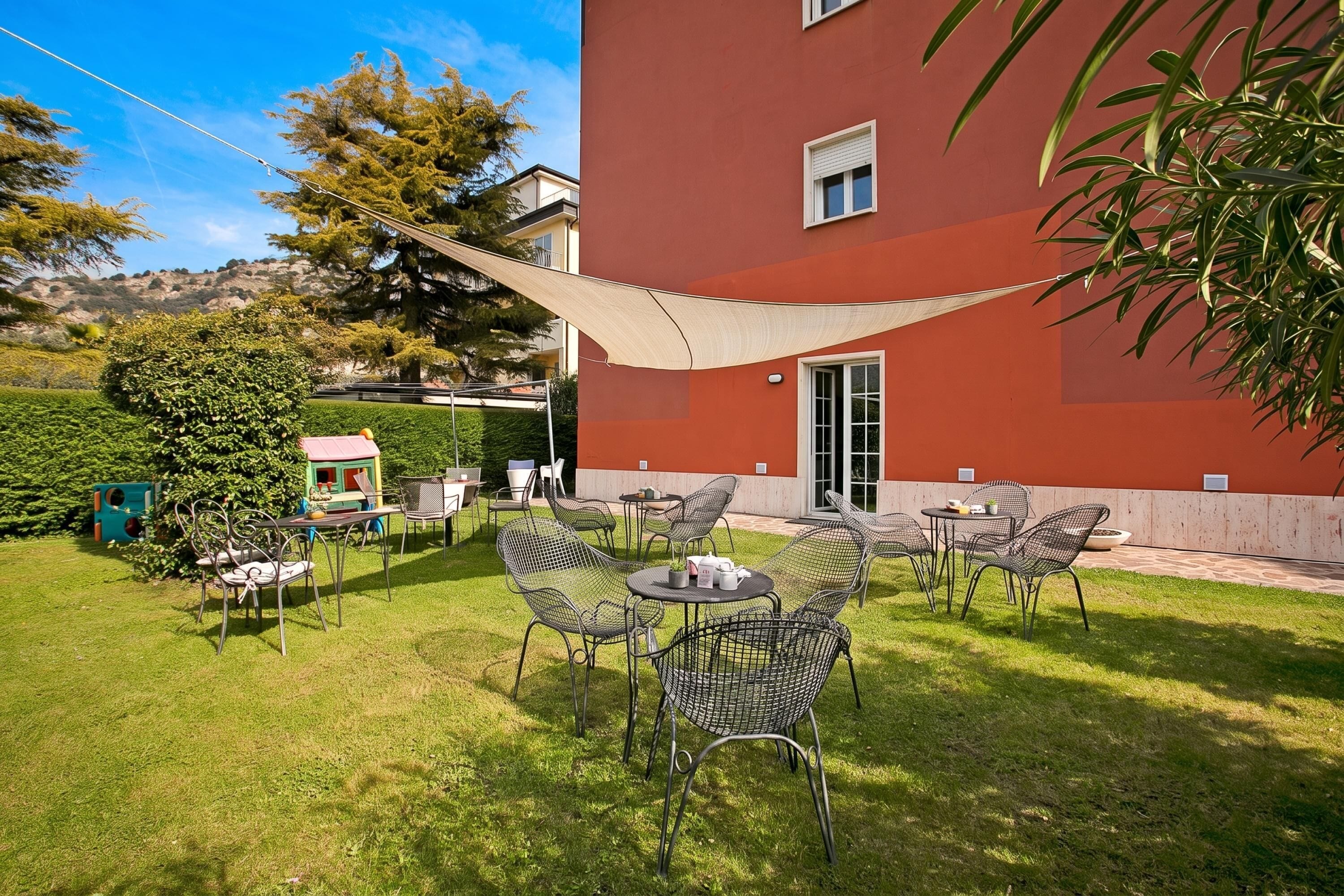 A patio area with outdoor furniture, a shade sail, and a building with a red exterior.