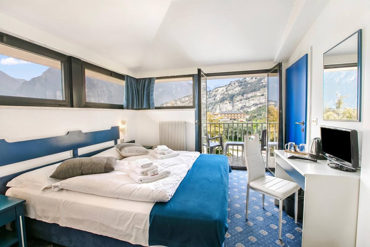 A hotel room with a bed, a desk, a chair, a TV, and a view of mountains.