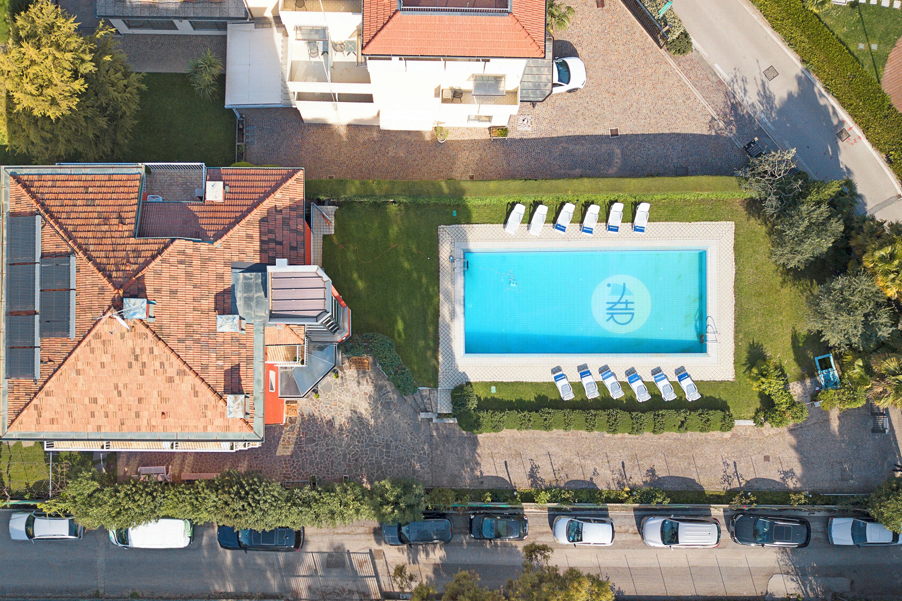 An aerial view of a property with a swimming pool, multiple cars parked, and a building with a tiled roof.
