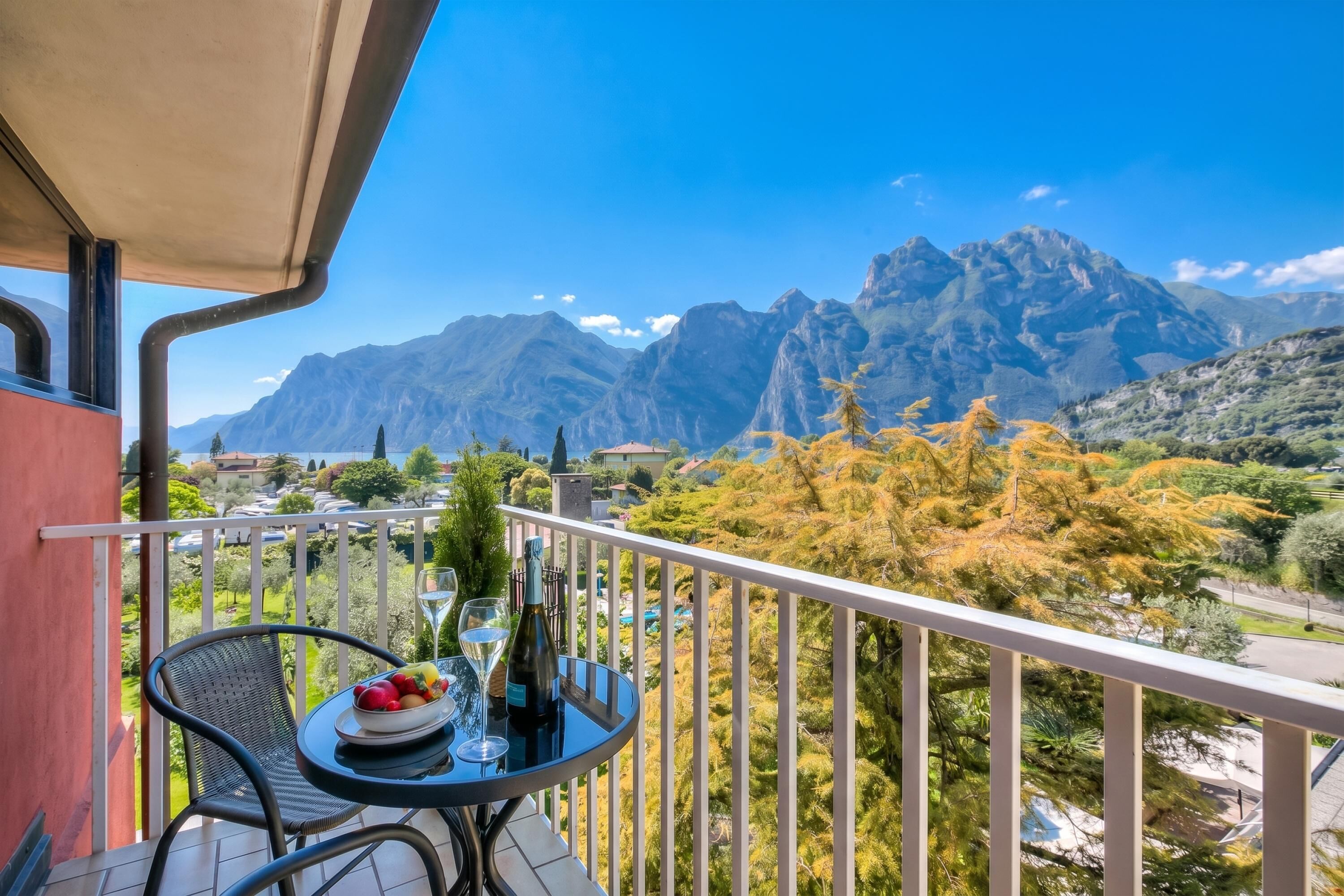A balcony with a table, a bottle, and glasses, overlooking a mountainous landscape.