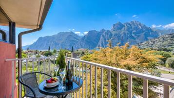A balcony with a table, a bottle, and glasses, overlooking a mountainous landscape.