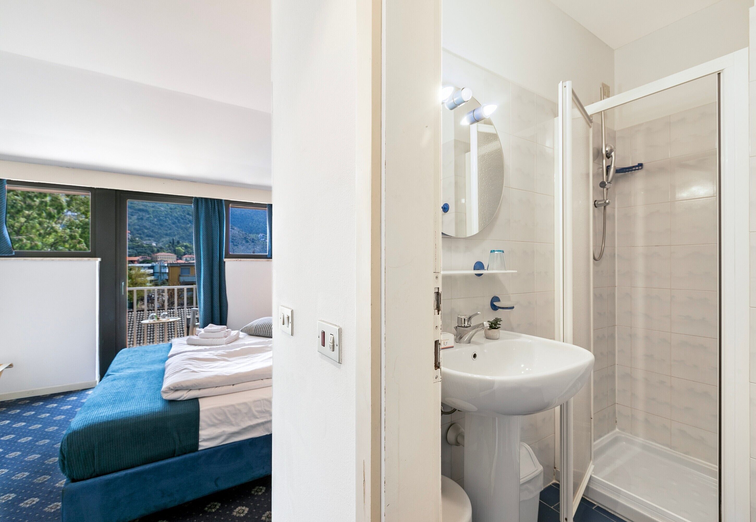 A hotel room with a bed, a bathroom with a sink and mirror, and a shower.