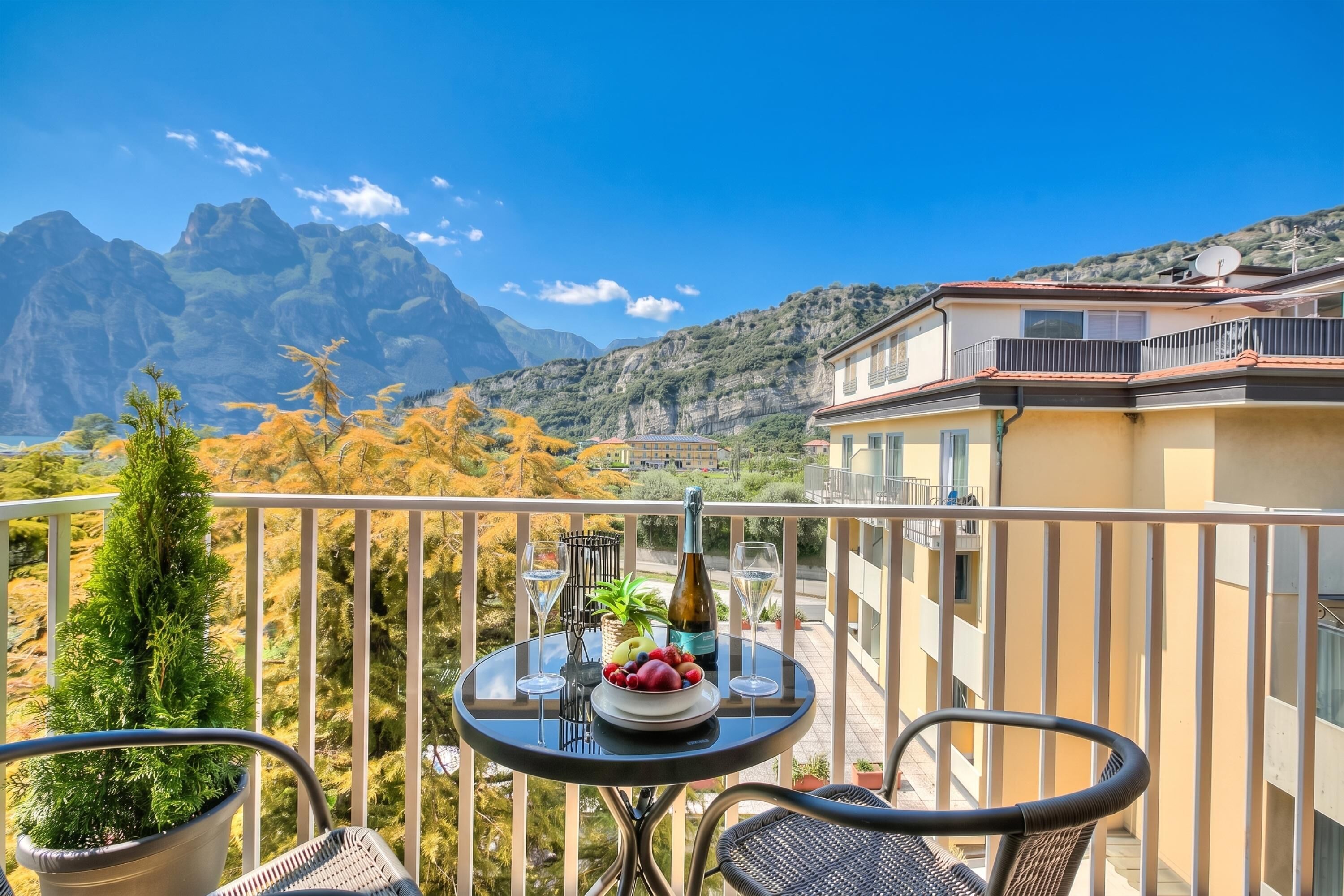 A balcony with a table set for two, a bottle, and a bowl of fruit.