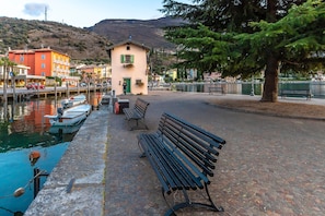 A waterfront promenade with benches, a small building, and boats docked by the water.