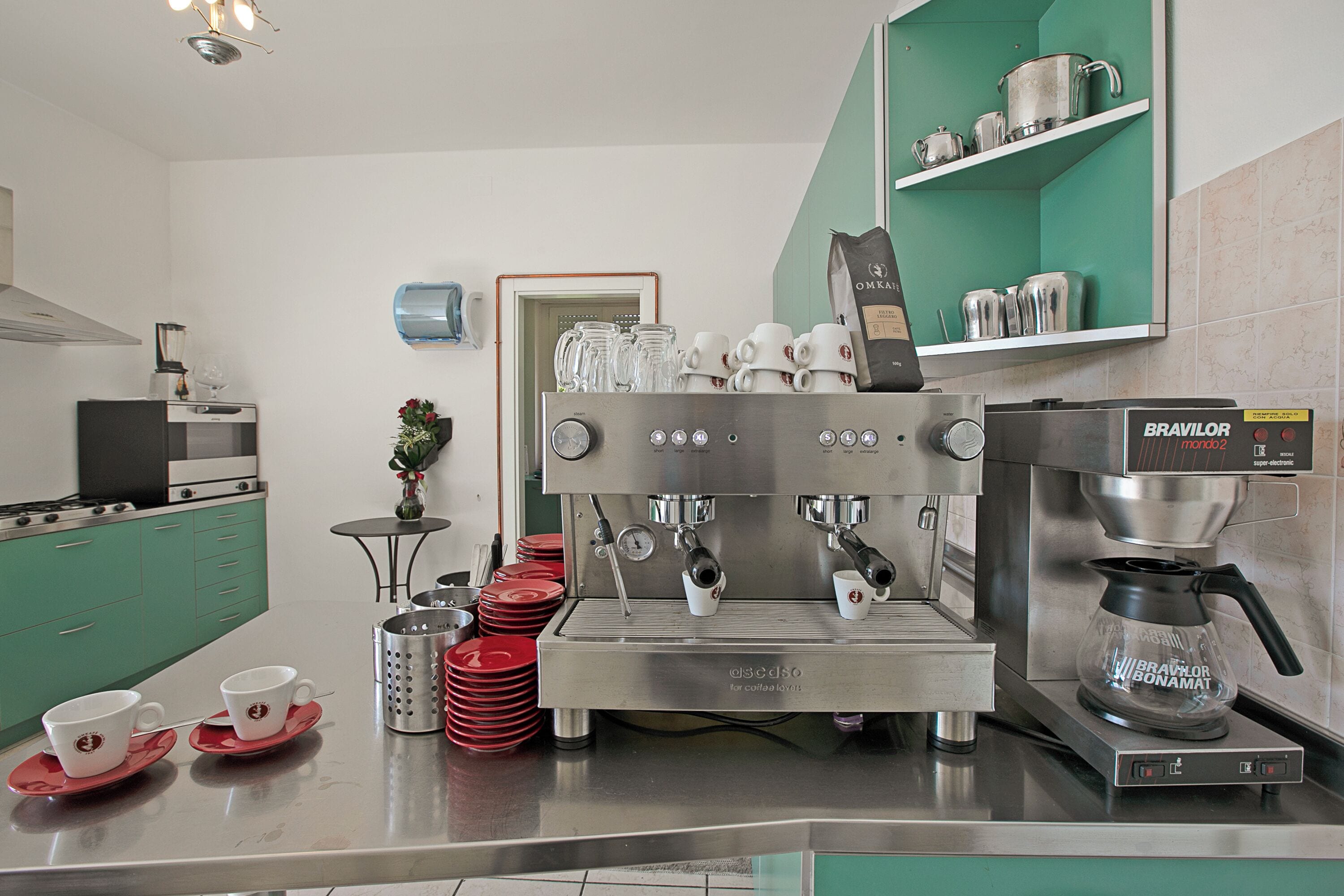A kitchen with a coffee machine, a coffee pot, and stacked cups.