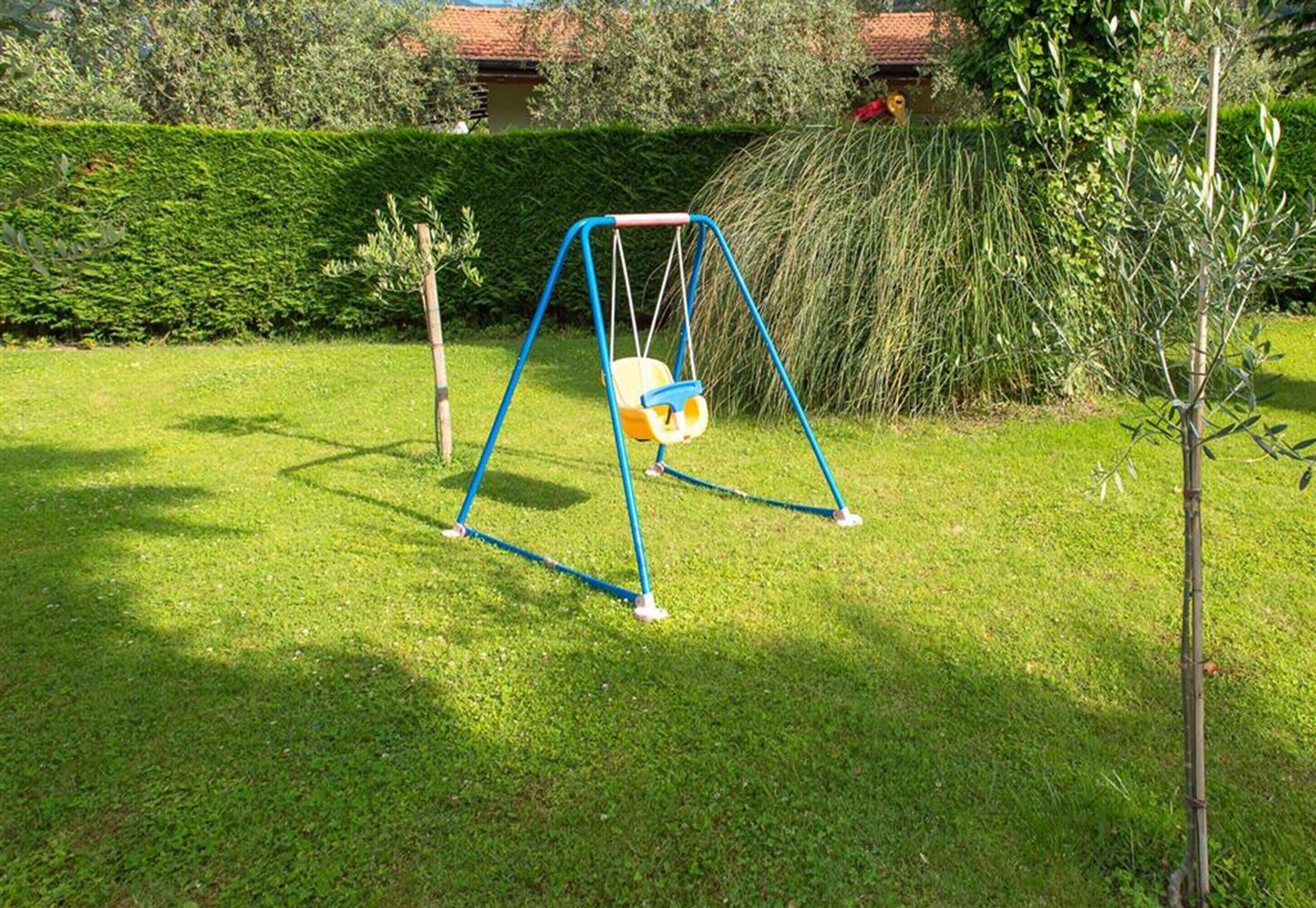 Eine Schaukel im grünen Garten, mit einer Hecke und Bäumen im Hintergrund.