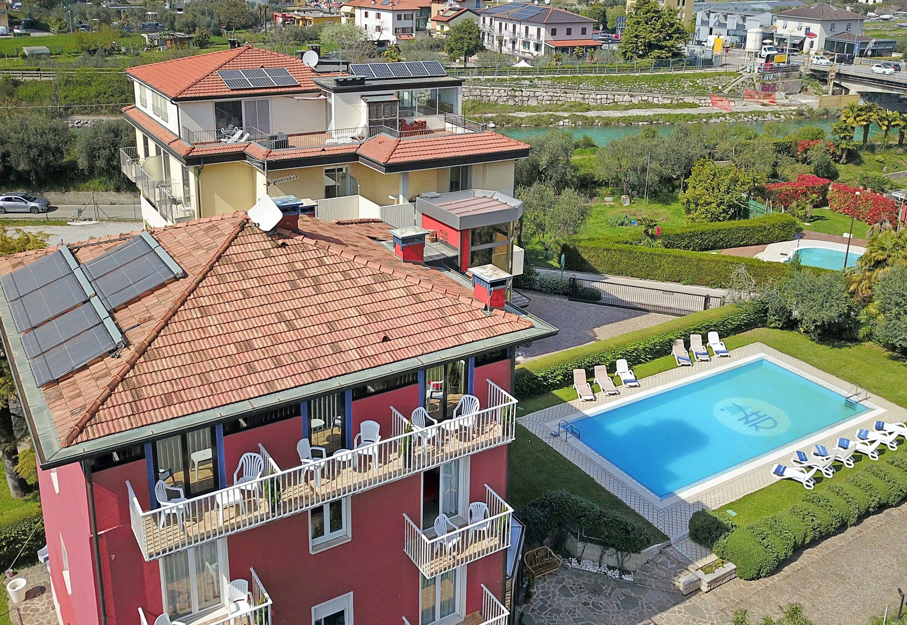 Uma casa de vários andares com um jardim no terraço, piscina e gramado bem cuidado.