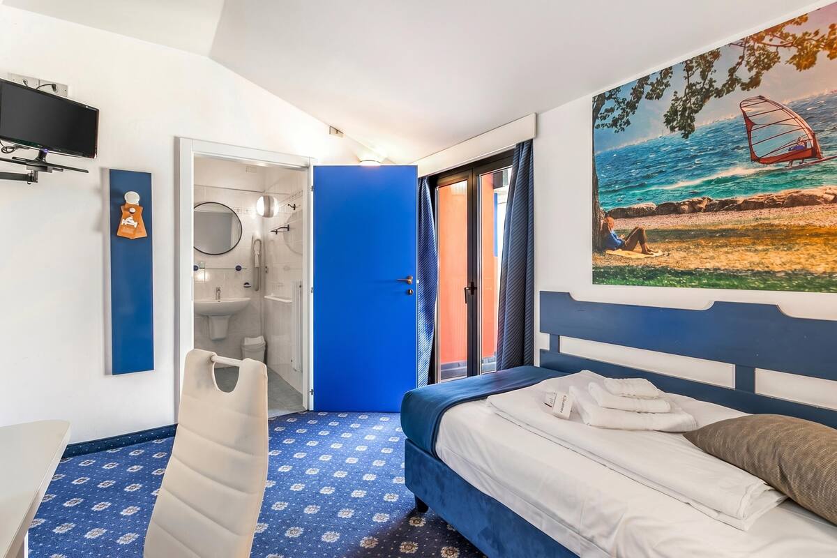A hotel room with a bed, a TV, a bathroom, and a painting of a beach scene.