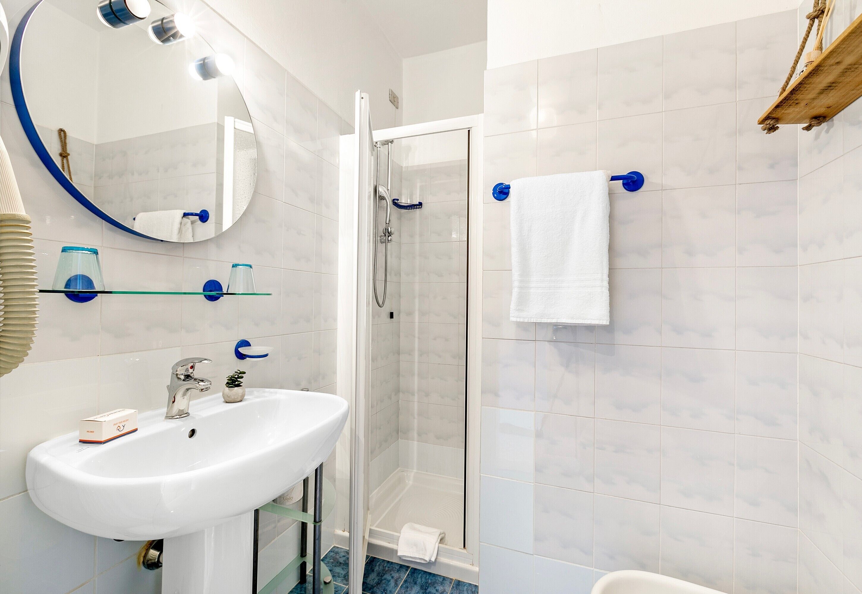 A bathroom with a white sink, a glass shower enclosure, and a white towel hanging on a blue towel rack.