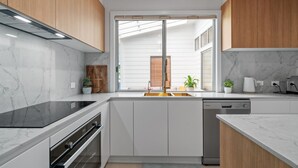 Una cocina moderna con armarios blancos, tope de cocción por inducción negro, lavavajillas y una ventana con persianas.