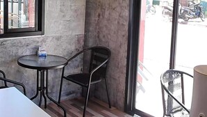A corner of a room with a round table and a chair, a window with a view of parked motorcycles, and a wall with two informational signs. - Samanta By The Hill (Koh Lan)