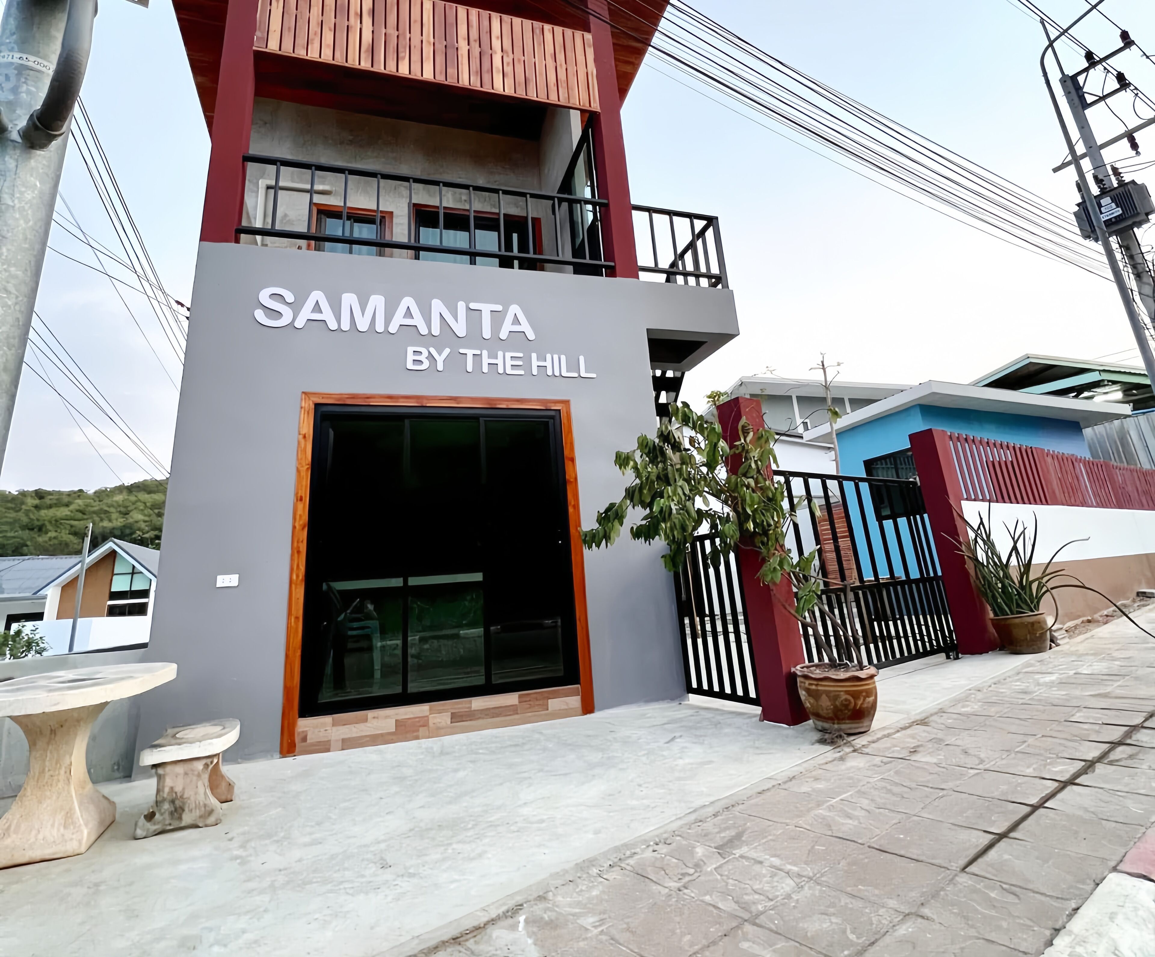 A building named "SAMANTA BY THE HILL" with a large entrance, a balcony, and potted plants outside.