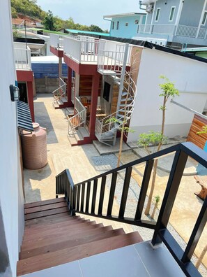 A multi-level residential building with a staircase, outdoor seating area, and a small tree. - Samanta By The Hill (Koh Lan)