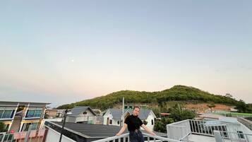 A person on a balcony with a view of a residential area and a hill in the background.