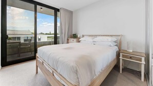 Une chambre avec un grand lit, une table de chevet, une chaise et une porte-fenêtre coulissante donnant sur un espace extérieur.