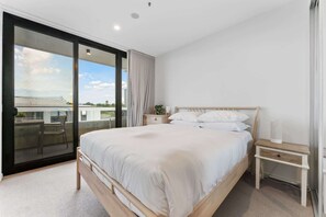 A bedroom with a large bed, a nightstand, a chair, and a sliding glass door leading to an outdoor area.