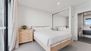 Une chambre à coucher moderne avec un lit en bois, une table de chevet agrémentée d’une plante et un grand miroir.