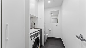 Une salle de bain moderne équipée d’un lave-linge, d’un évier, de toilettes et d’un miroir.