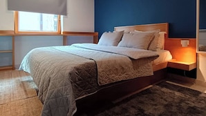 Un dormitorio con cama, mesita de noche, ventana con persianas y una pared de acento azul.