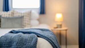 A bedroom with a bed, pillows, a bedside table with a lamp, and a window with curtains. - Charming Downtown Bungalow with Yard & Gas Grill (Oshkosh)