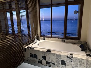 A bathroom with a large bathtub, a window with a view of the sea, and a tiled floor. - Hotel CASA VICO (Ako)