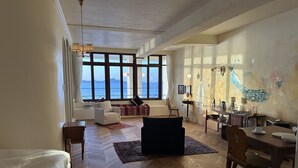Un salón comedor espacioso con un gran ventanal con vista al mar, suelo de madera y una mesa con sillas.