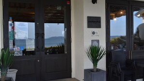 Entrada de un hotel con vista al mar, un letrero que anuncia un restaurante cercano y una placa en la pared.