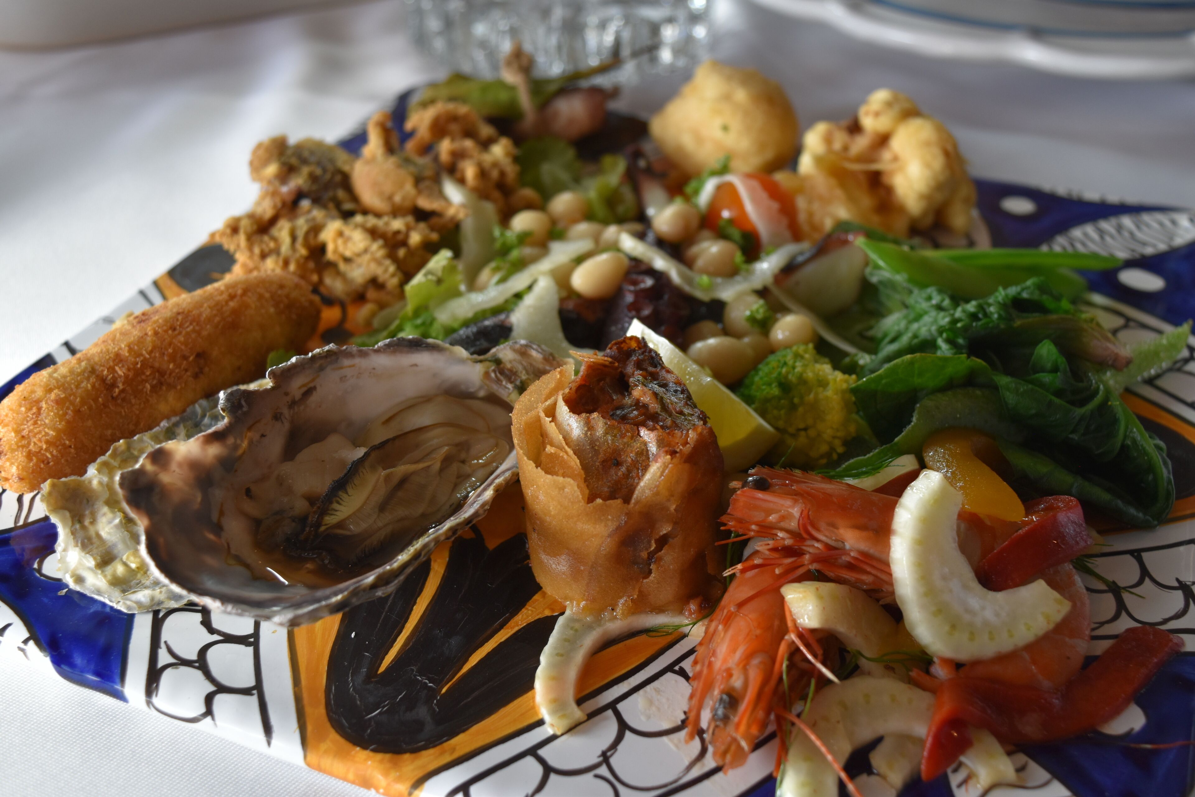 A seafood platter with various items including shrimp, mussels, and a breaded item, served on a decorative plate.