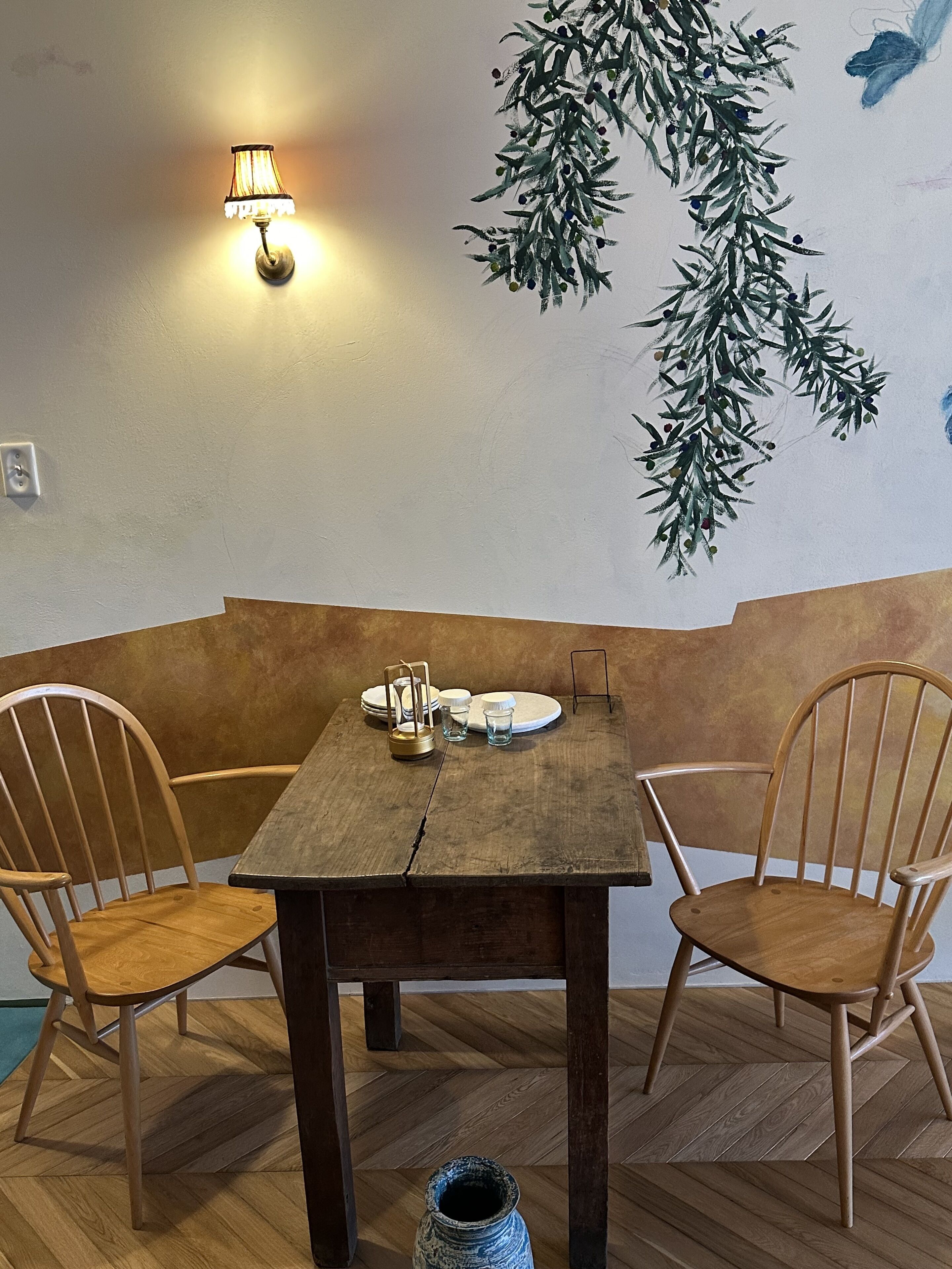 Una mesa de madera con sillas, una lámpara fijada en la pared y una rama decorativa.