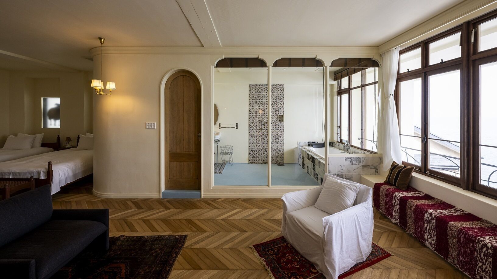 Hotelkamer met een groot bed, een bank, een stoel, een spiegel en uitzicht op de stad door grote ramen.