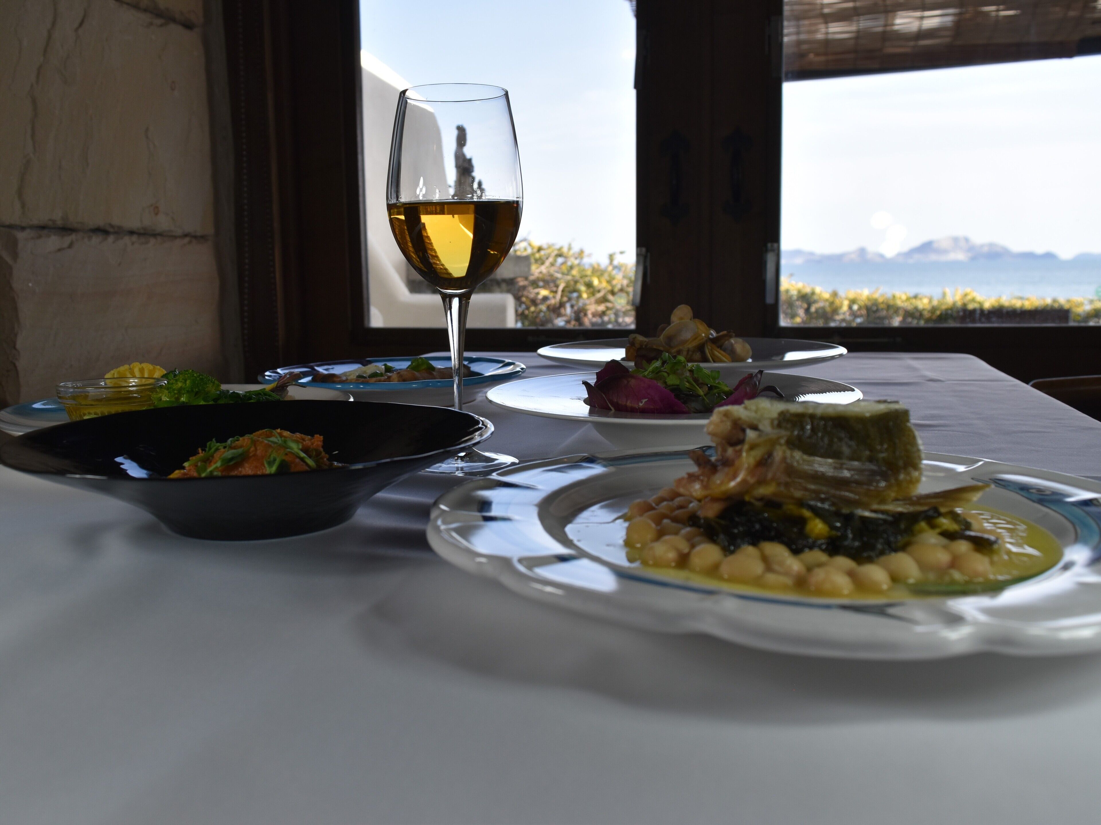 Mesa lista para una comida con varios platos y una copa de vino, con vistas a un paisaje montañoso.