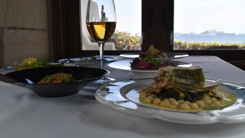 Mesa lista para una comida con varios platos y una copa de vino, con vistas a un paisaje montañoso.